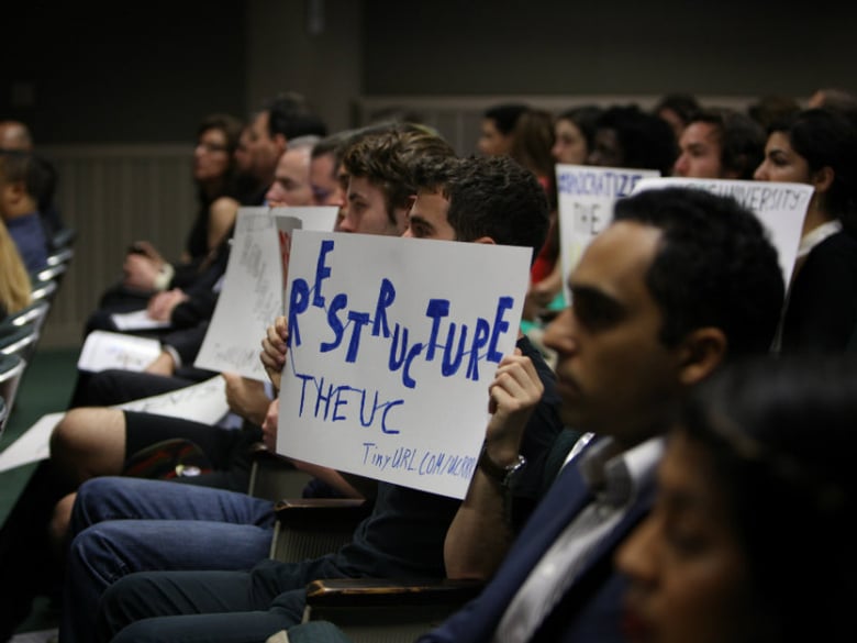 Protesters hold signs during a California Assembly hearing on the critical audit of the UC Office of the President on Tuesday, May 2, 2017.